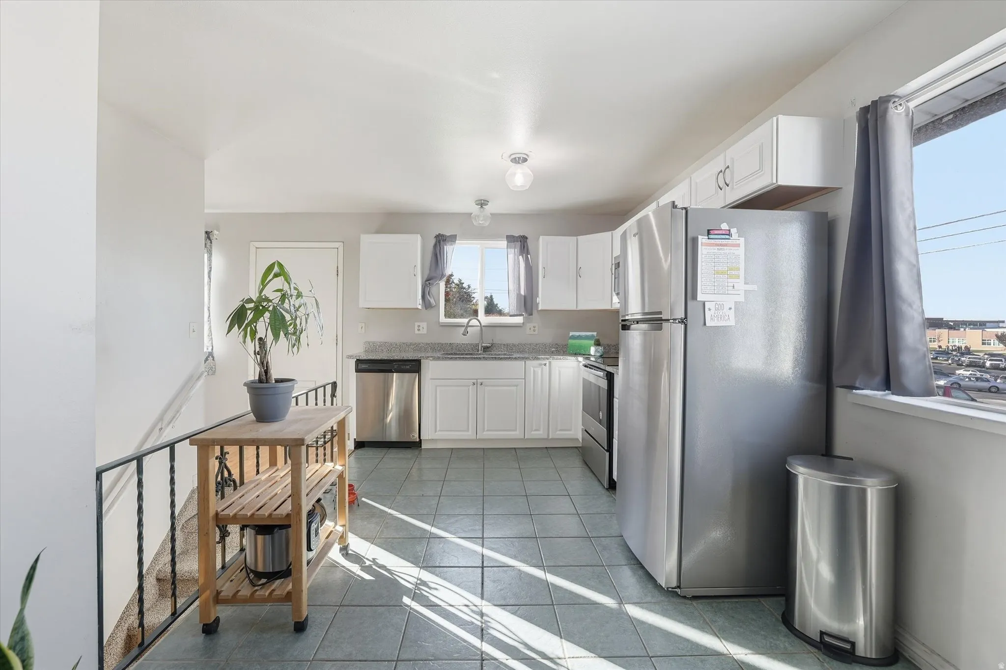 Kitchen featuring appliances with stainless steel finishes, white cabinetry, dark tile patterned flooring, and light stone countertops