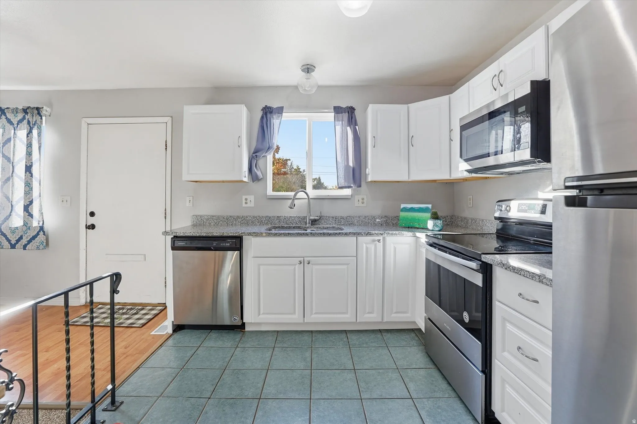 Kitchen with appliances with stainless steel finishes, white cabinetry, light tile patterned floors, and light stone countertops