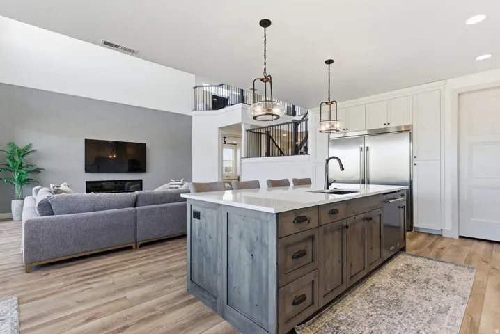 Kitchen featuring white cabinets, light wood-type flooring, pendant lighting, an island with sink, and dark brown cabinetry