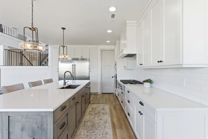 Kitchen with a kitchen bar, white cabinets, hanging light fixtures, appliances with stainless steel finishes, and dark wood-style flooring