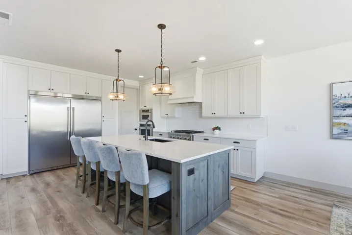 Kitchen with appliances with stainless steel finishes, white cabinets, pendant lighting, a kitchen breakfast bar, and decorative backsplash