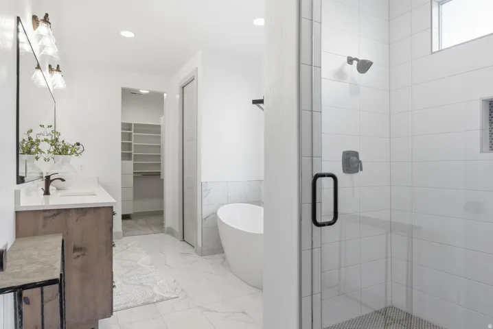 Full bath with a spacious closet, a freestanding tub, double vanity, light marble finish floors, and a stall shower