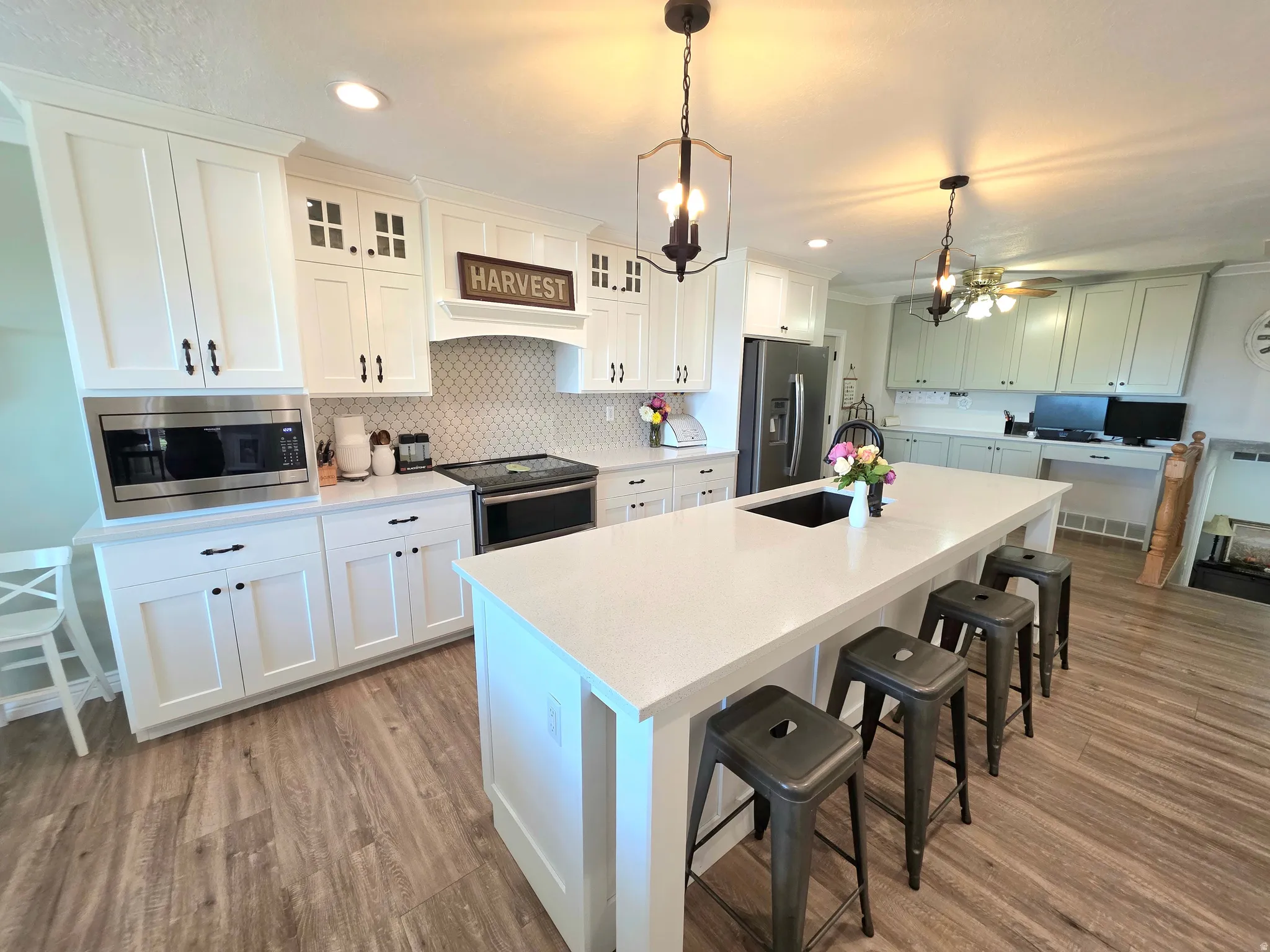 Kitchen with a breakfast bar area, light wood finished floors, backsplash, appliances with stainless steel finishes, and hanging light fixtures