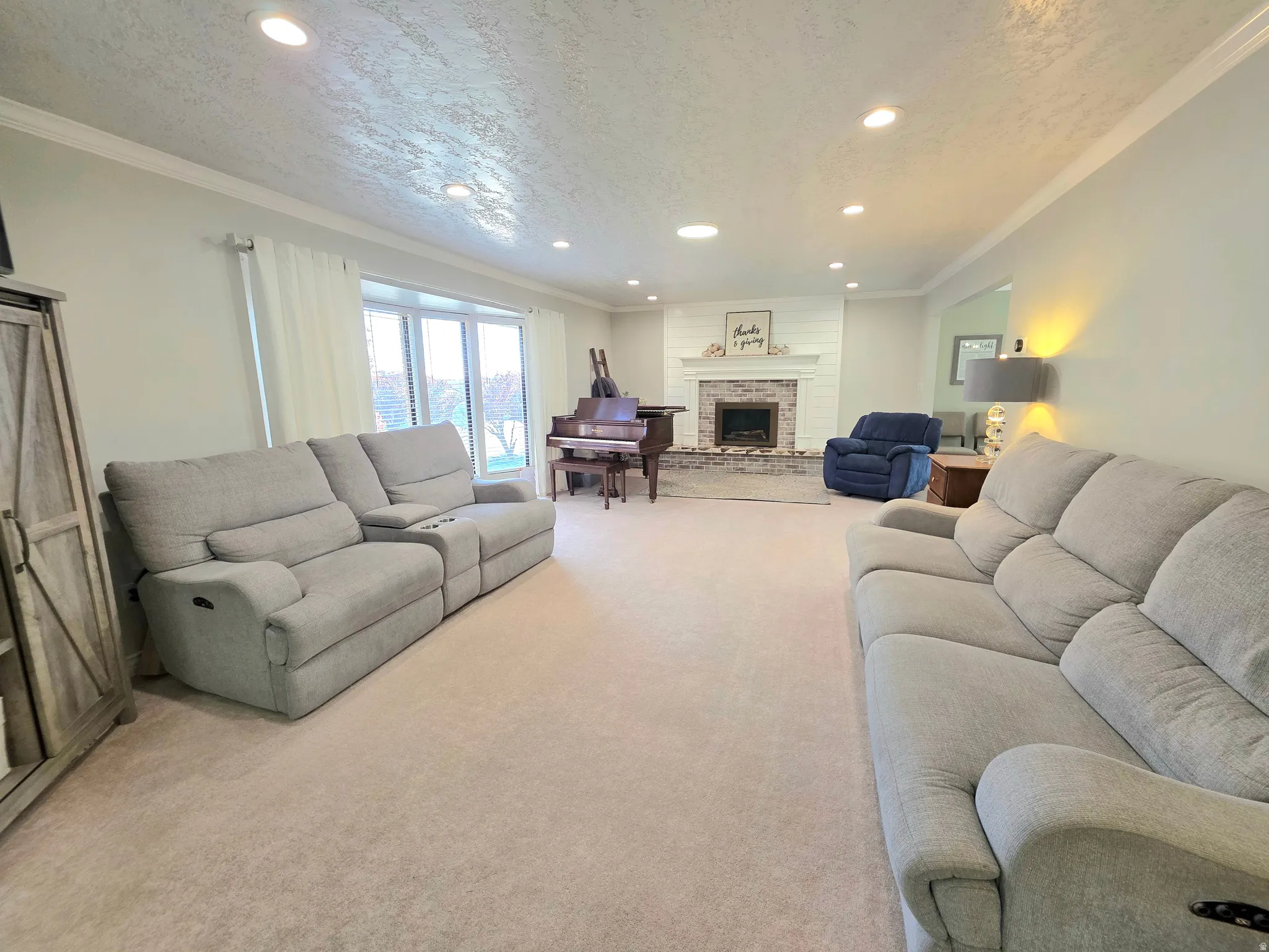 Living area with crown molding, a textured ceiling, light carpet, recessed lighting, and a fireplace