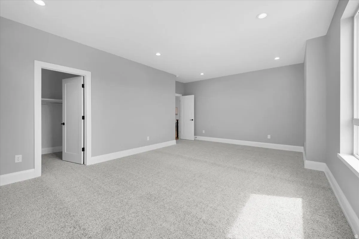 Unfurnished bedroom featuring light colored carpet, recessed lighting, and a walk in closet