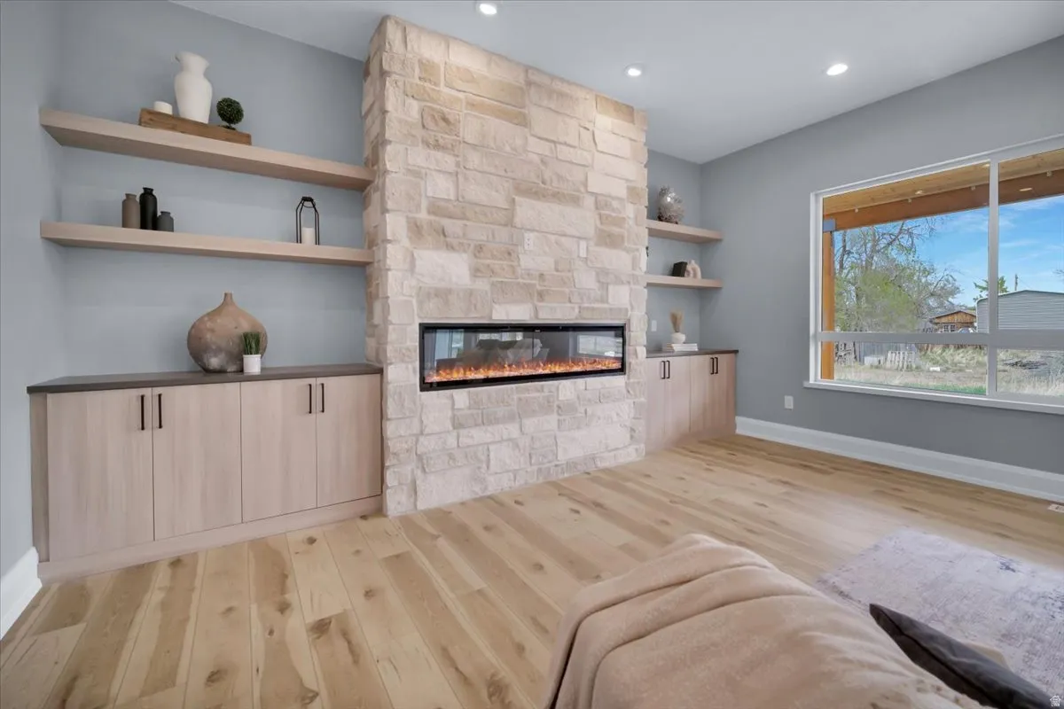 Living room with light wood-style floors, a stone fireplace, and recessed lighting