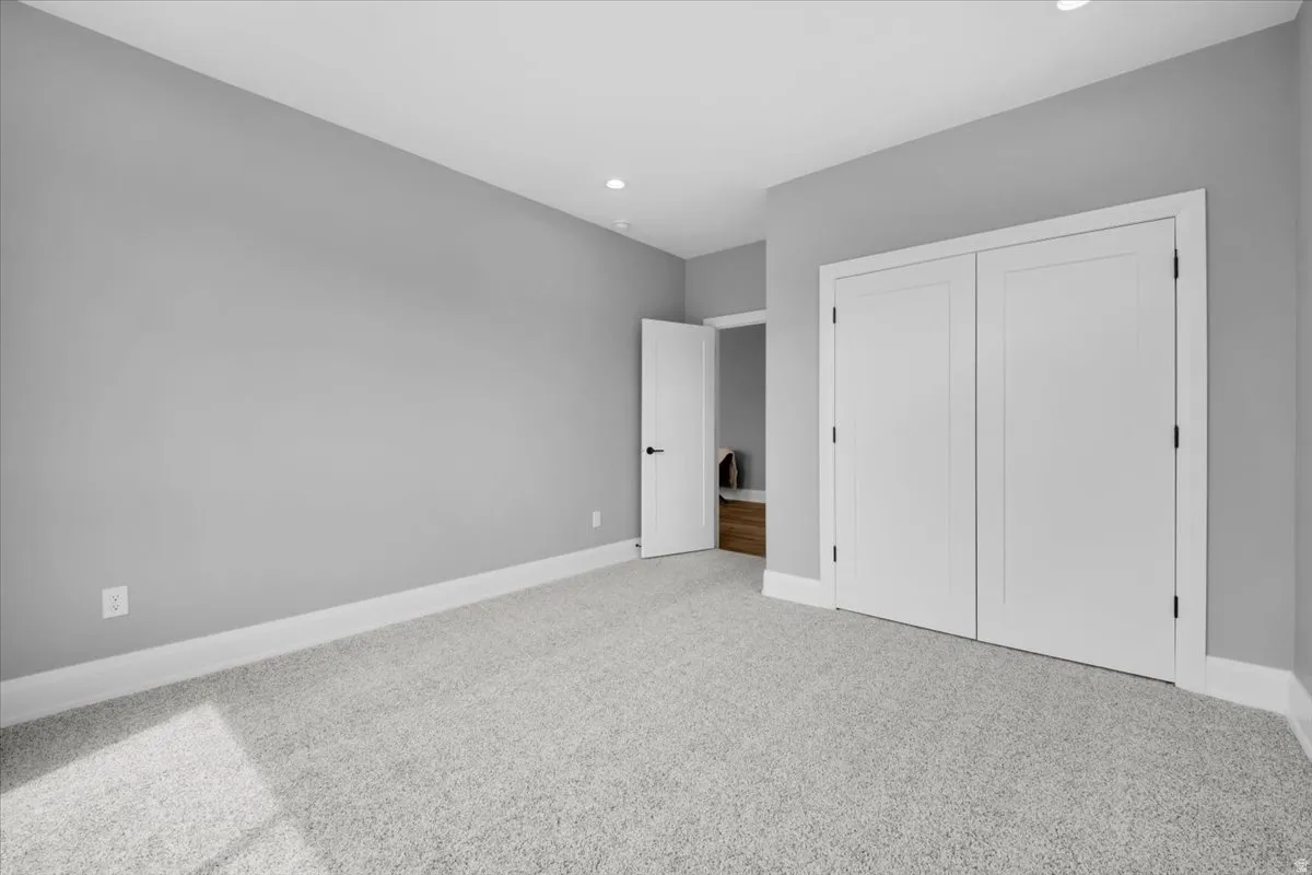 Unfurnished bedroom with light colored carpet, a closet, and recessed lighting