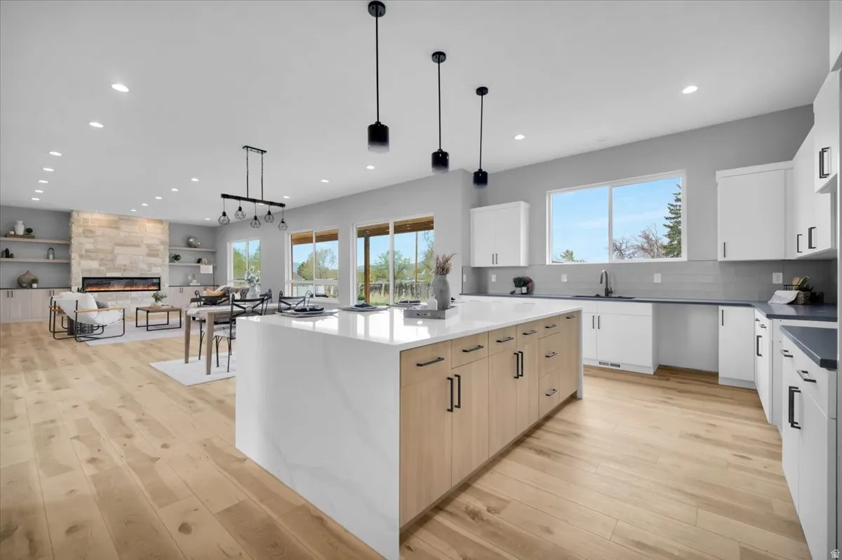Kitchen featuring dual tone cabinetry, a large island, a tiled fireplace, dark stone countertops, and light wood-type flooring