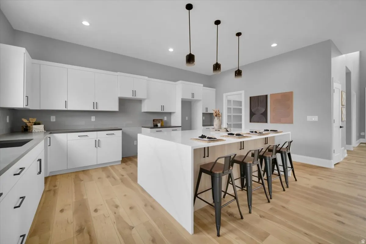 Kitchen featuring a kitchen bar, light wood-style flooring, white cabinets, a spacious island, and light stone counters