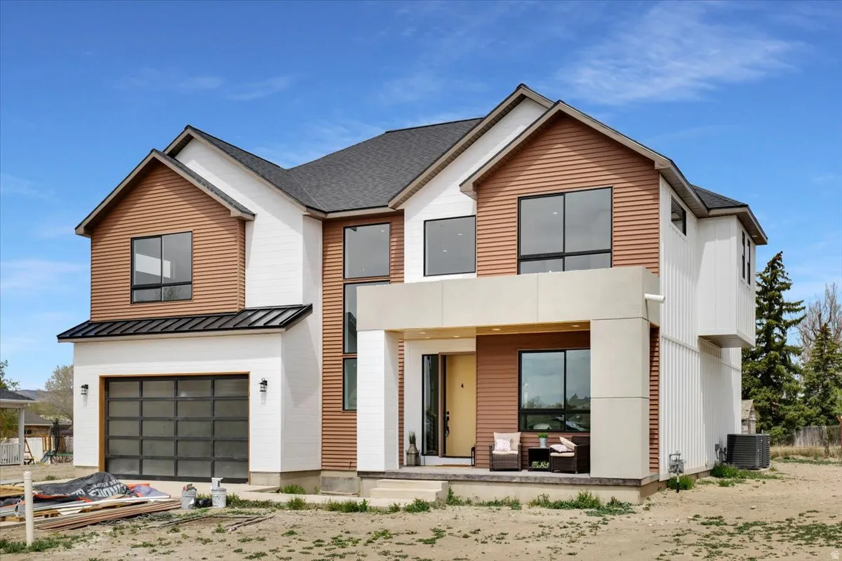 View of front of home with covered porch, an attached garage, a standing seam roof, and driveway