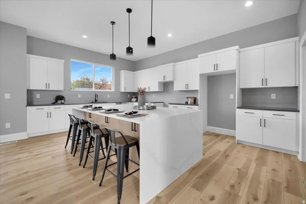Kitchen featuring a kitchen breakfast bar, white cabinetry, light wood finished floors, a kitchen island, and pendant lighting