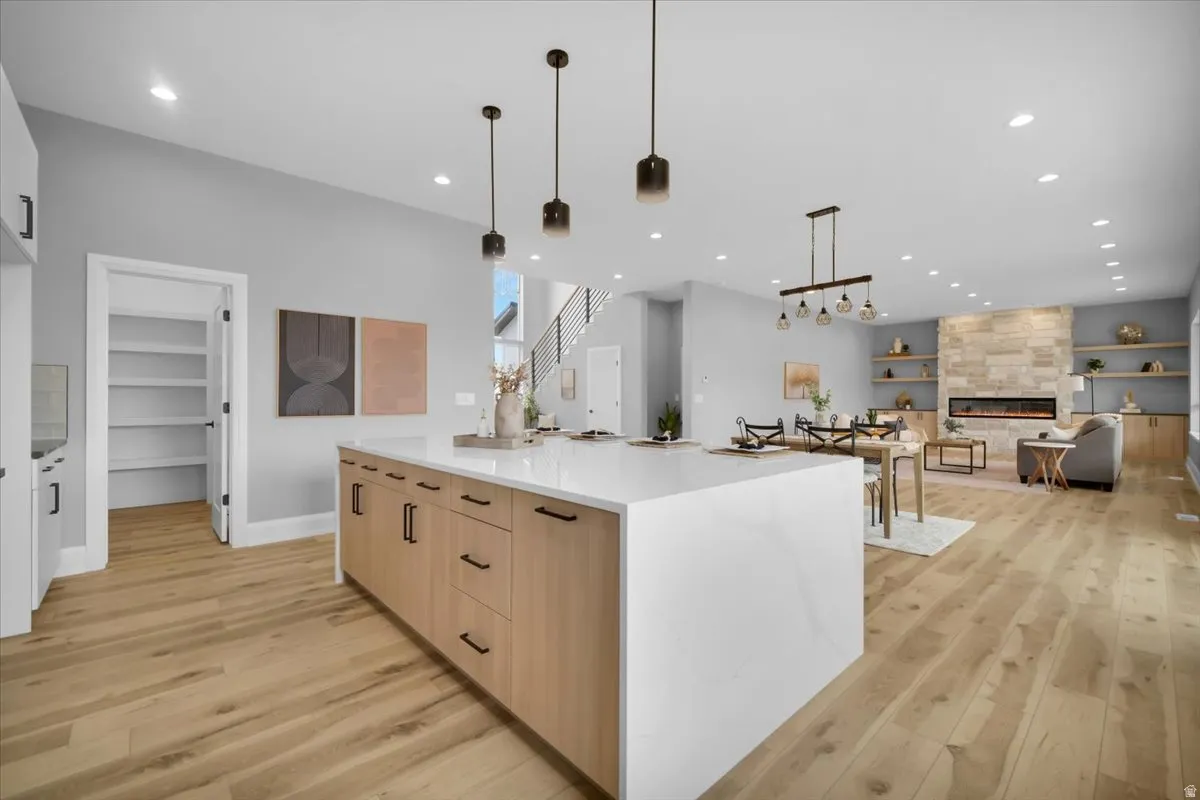 Kitchen featuring light wood finish cabinetry, light wood-style floors, a large island, light stone countertops, and open floor plan