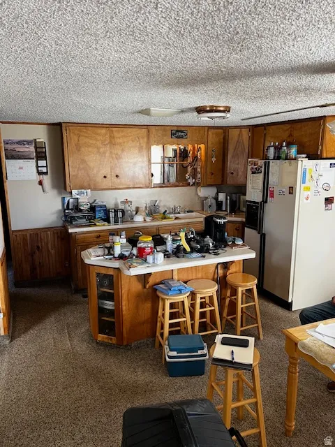 Kitchen with white refrigerator with ice dispenser, a kitchen breakfast bar, light countertops, wood walls, and a wainscoted wall