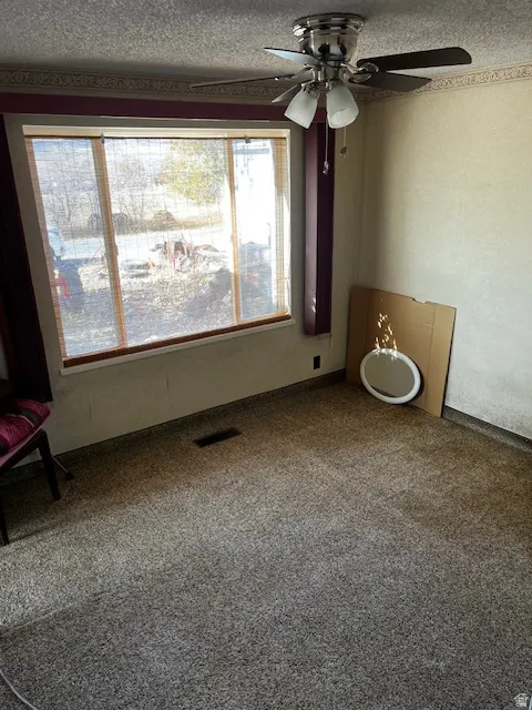 Carpeted spare room featuring a textured ceiling and ceiling fan