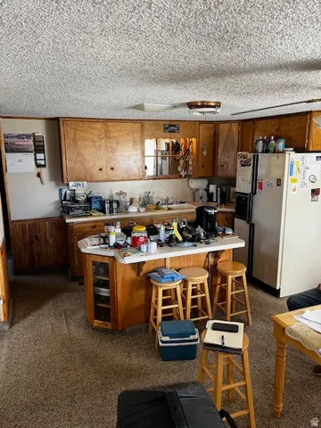 Kitchen with white refrigerator with ice dispenser, a kitchen breakfast bar, light countertops, wood walls, and a wainscoted wall