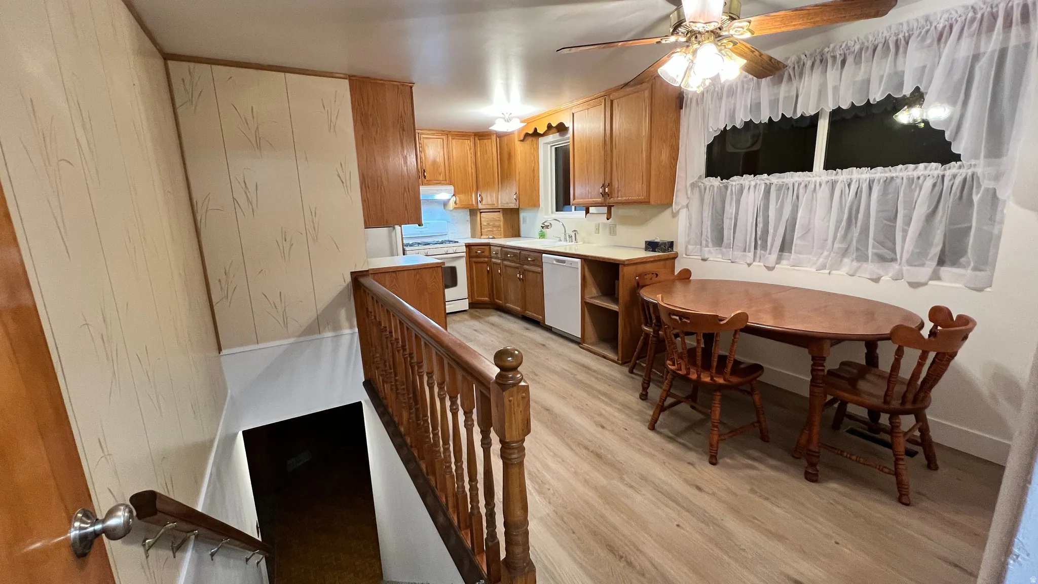 Kitchen with light countertops, light wood finished floors, brown cabinetry, white appliances, and a ceiling fan