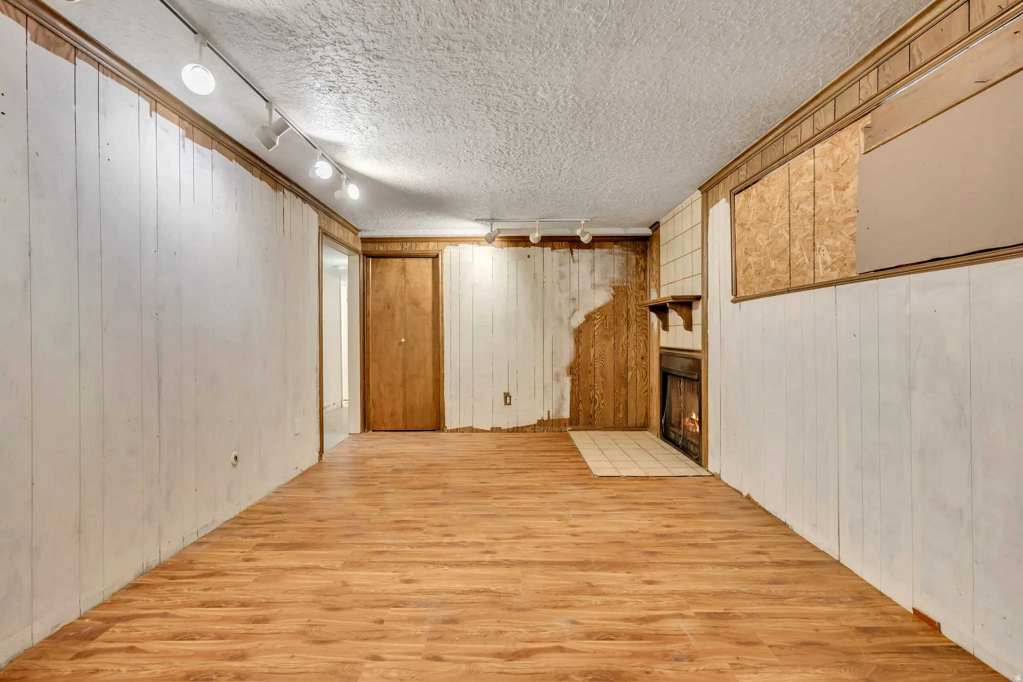 Finished basement featuring wood walls, light wood finished floors, track lighting, a fireplace, and a textured ceiling
