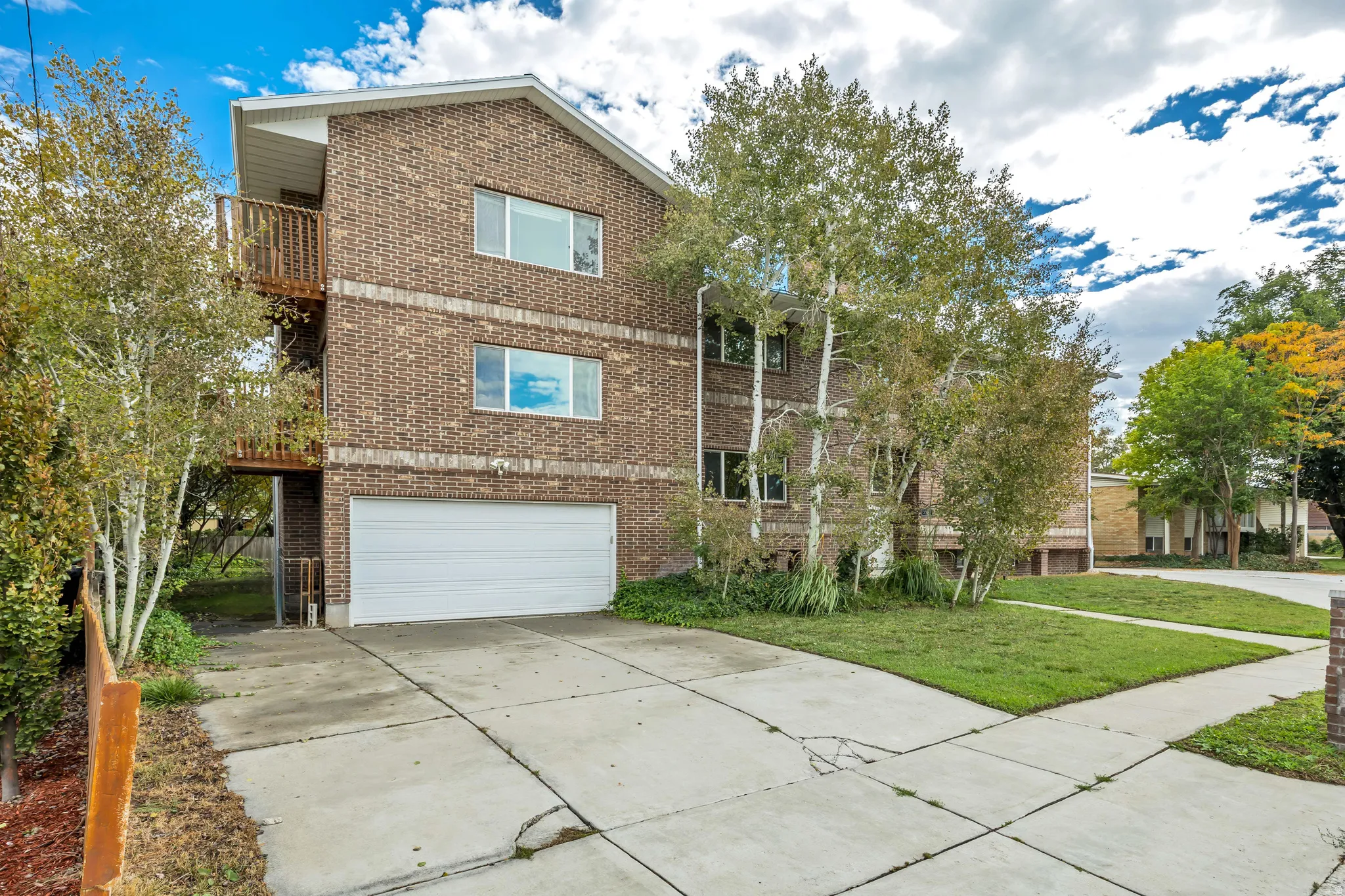 View of front facade featuring brick siding, a front lawn, driveway, a garage, and a balcony