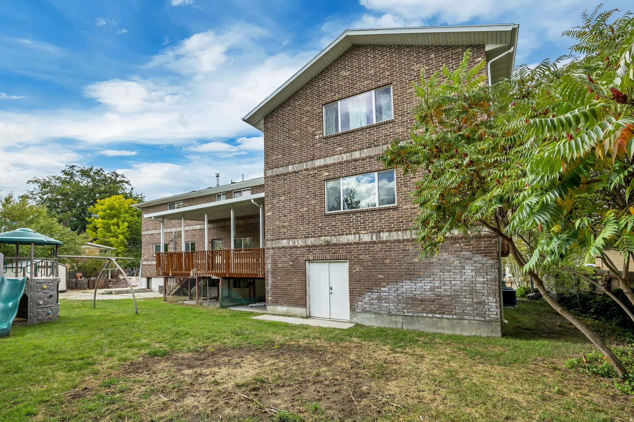 Back of house with a lawn, brick siding, a playground, a patio, and a deck