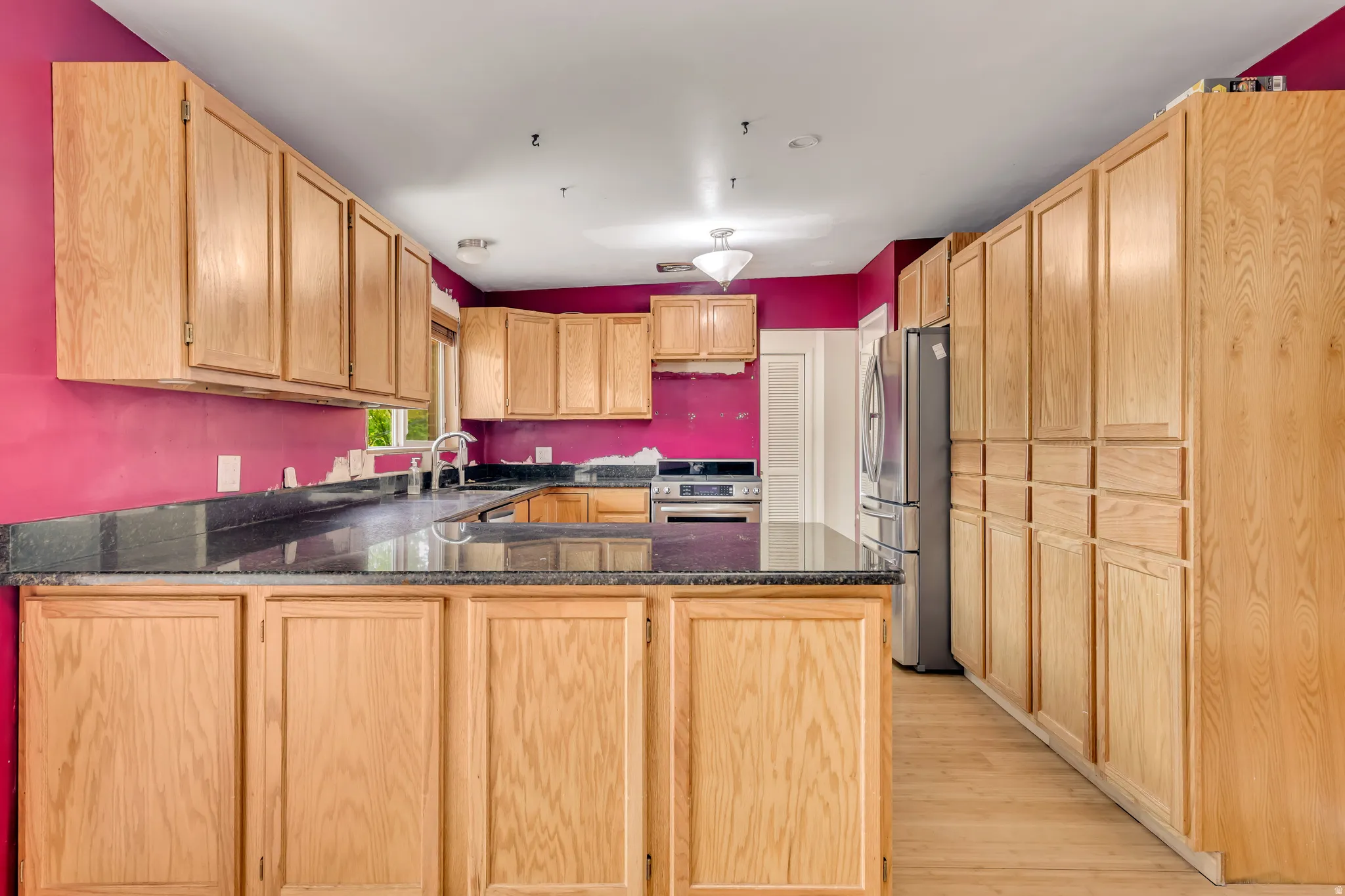 Kitchen with light brown cabinets, a peninsula, appliances with stainless steel finishes, light wood-style flooring, and dark stone countertops