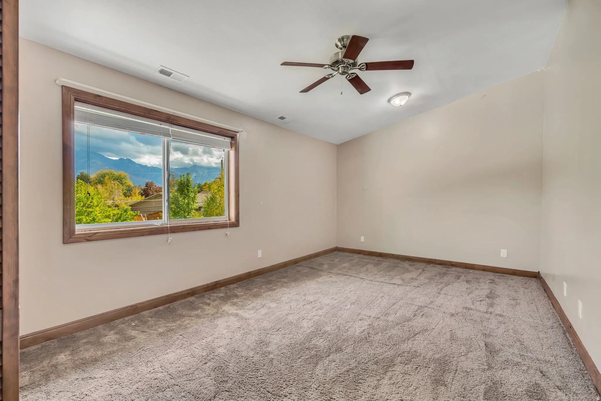 Empty room with a mountain view, light colored carpet, and a ceiling fan
