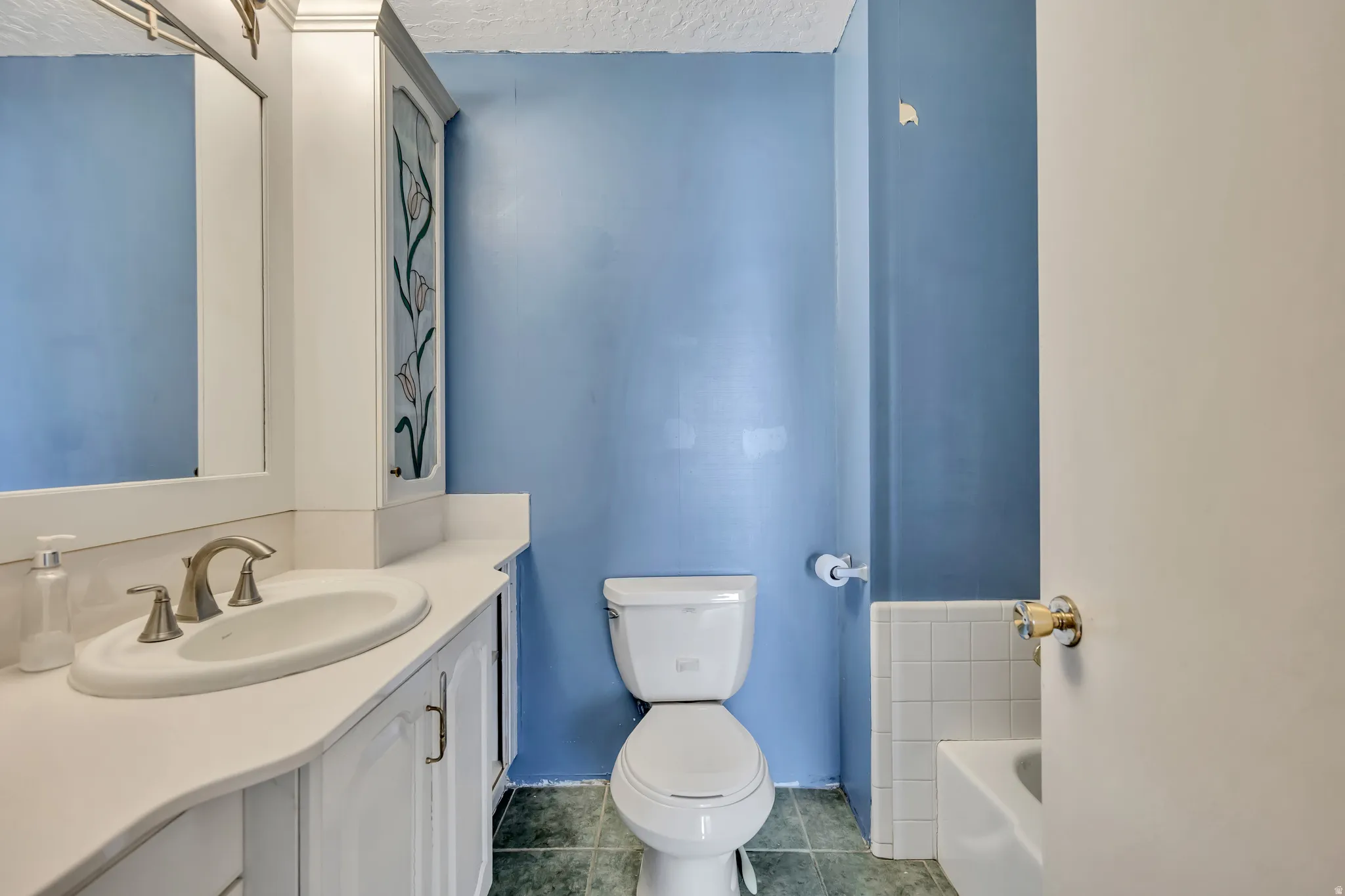 Full bathroom with a textured ceiling, dark tile patterned flooring, vanity, and a bathtub