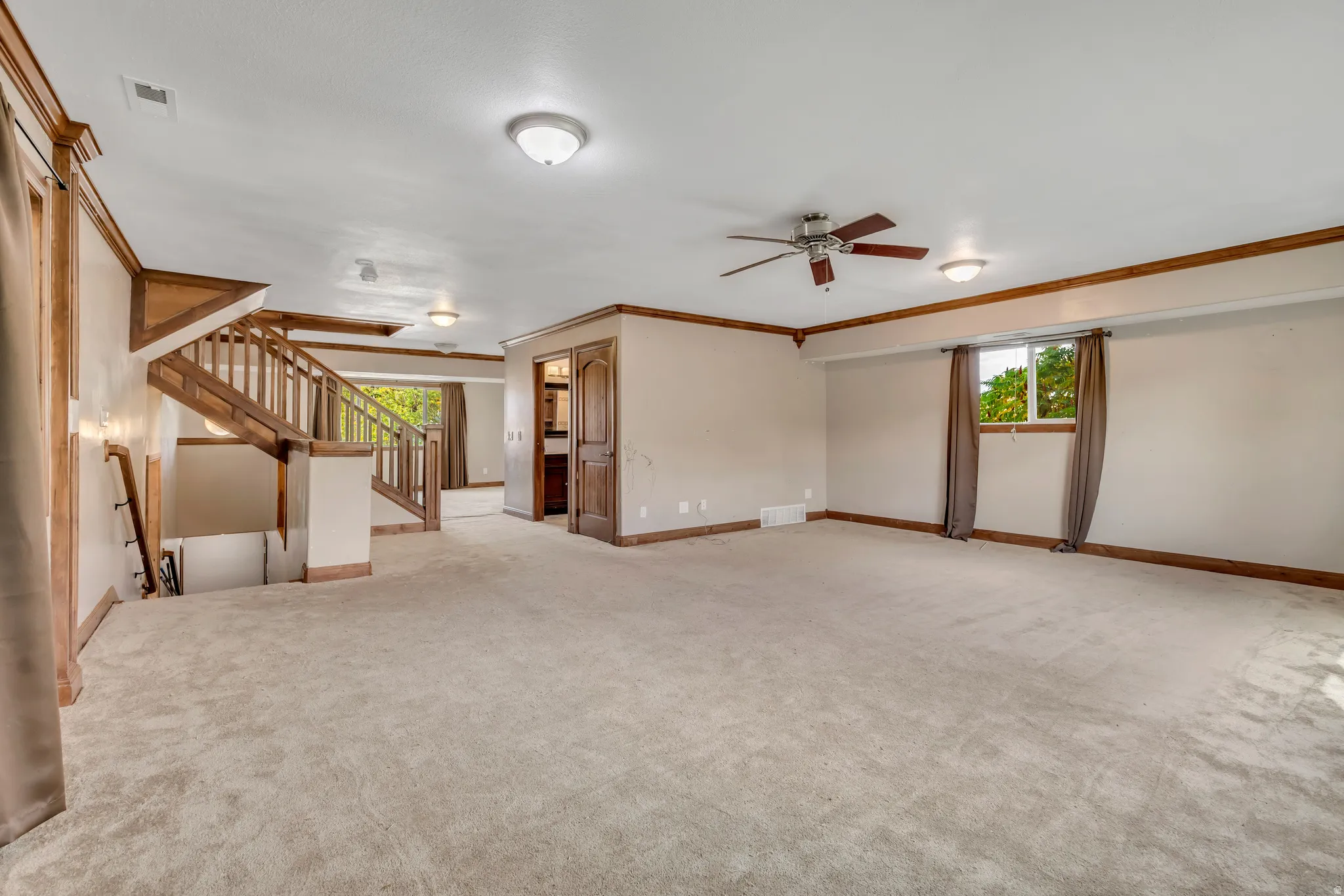 Unfurnished living room with crown molding, a ceiling fan, light colored carpet, and stairway