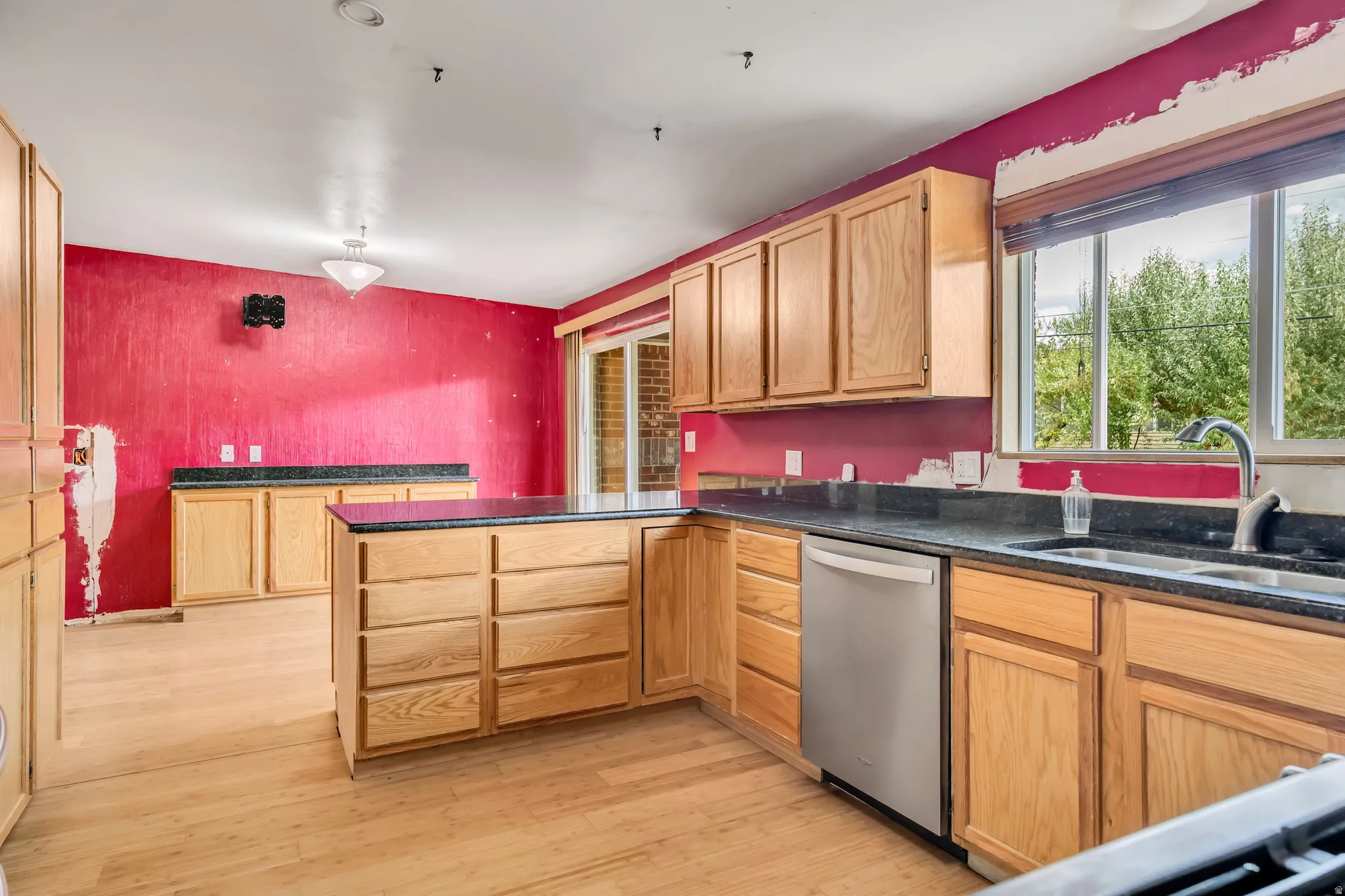 Kitchen with a peninsula, stainless steel dishwasher, light wood finished floors, light brown cabinets, and dark stone counters