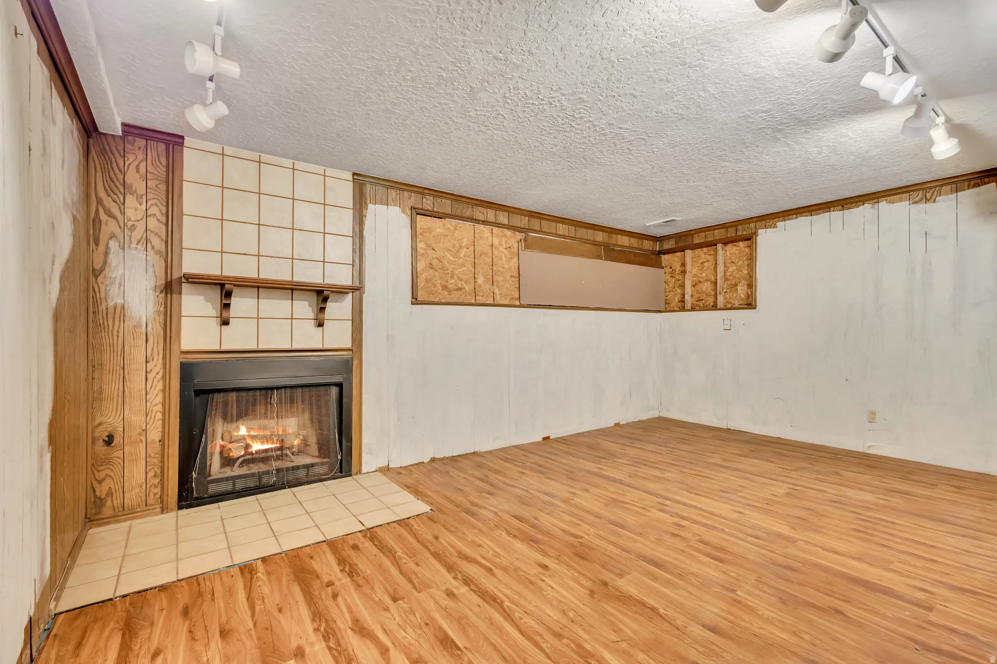 Unfurnished living room with rail lighting, a tiled fireplace, light wood-type flooring, and a textured ceiling