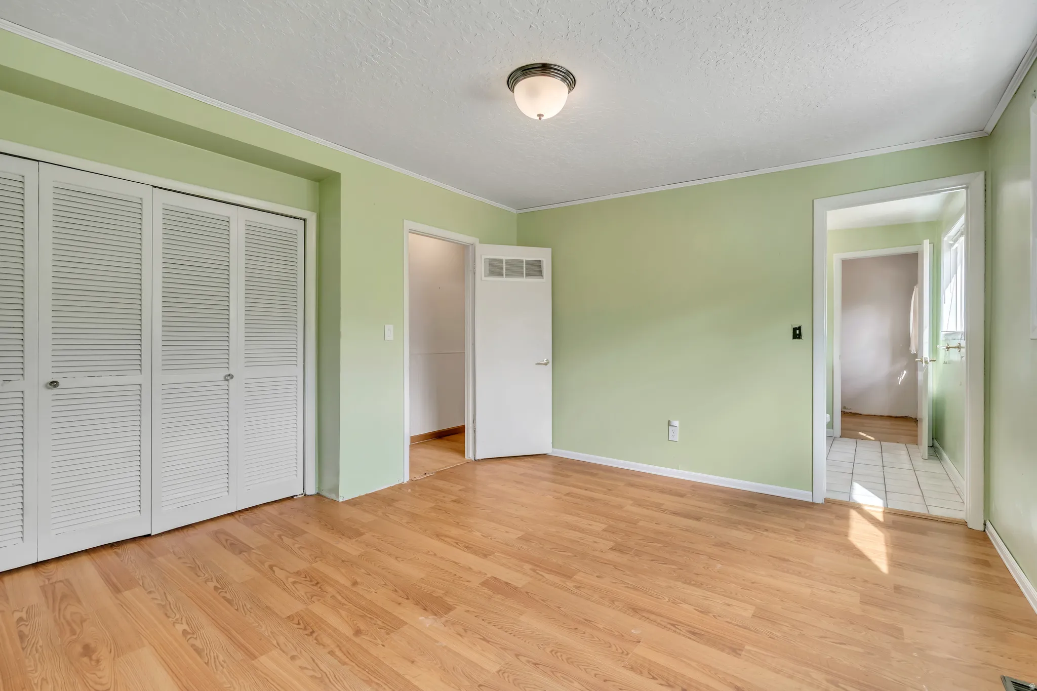 Unfurnished bedroom featuring light wood-style floors, a textured ceiling, a closet, and crown molding
