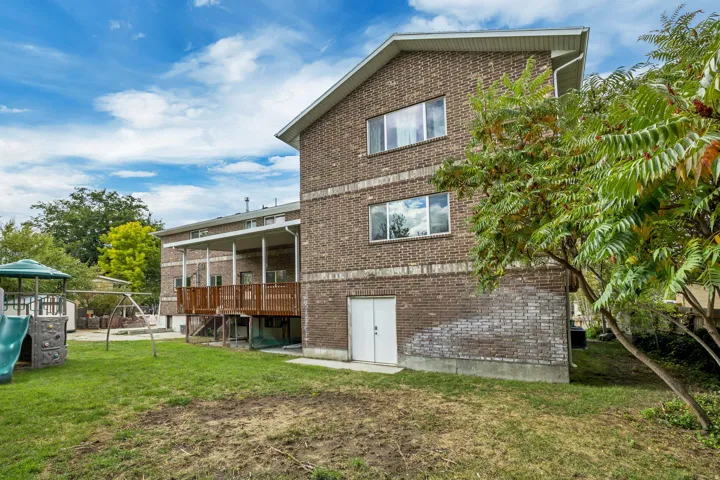 Back of house with a lawn, brick siding, a playground, a patio, and a deck