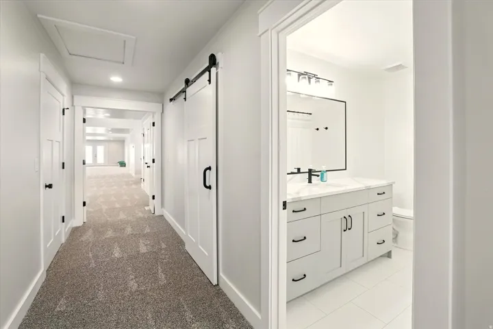 Corridor with light carpet, a barn door, light tile patterned flooring, recessed lighting, and attic access