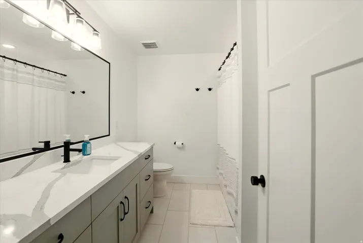 Full bathroom featuring light tile patterned floors, curtained shower, and vanity