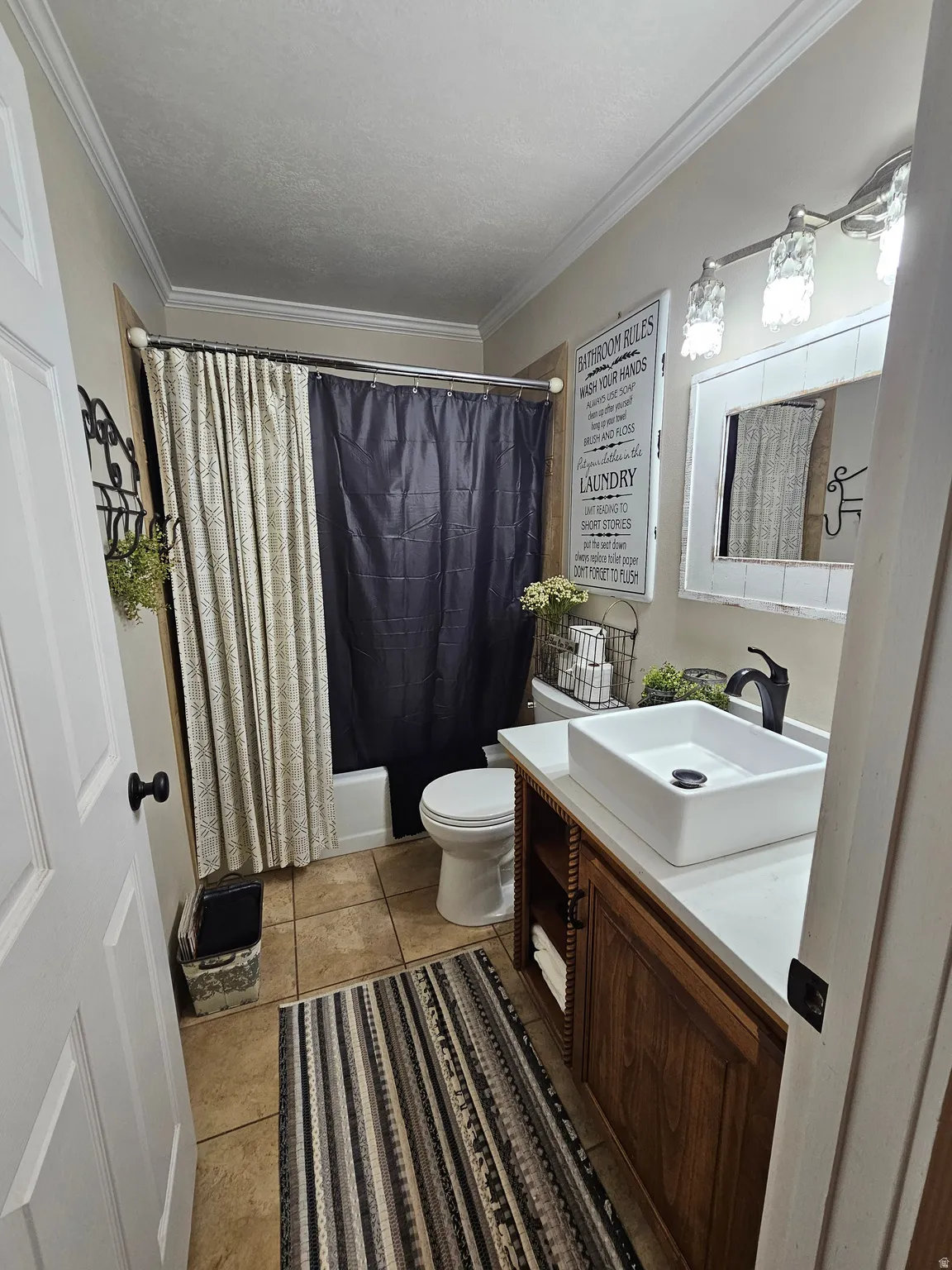 Full bathroom with vanity, crown molding, light tile patterned flooring, shower / bath combo with shower curtain, and a textured ceiling