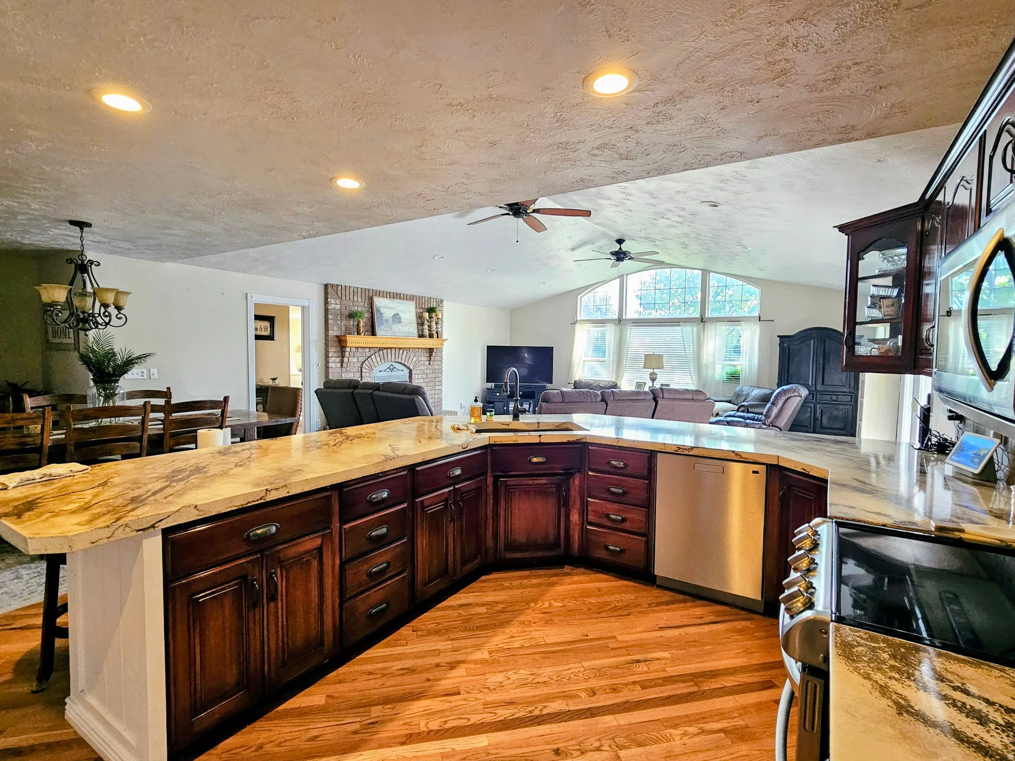 Kitchen with open floor plan, appliances with stainless steel finishes, light wood finished floors, light countertops, and a textured ceiling