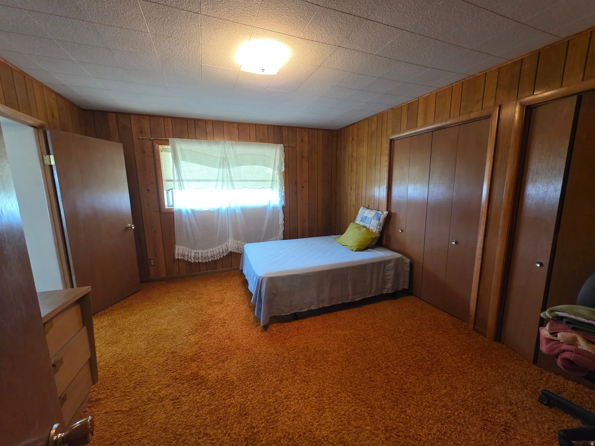 Bedroom featuring light carpet, wooden walls, and two closets