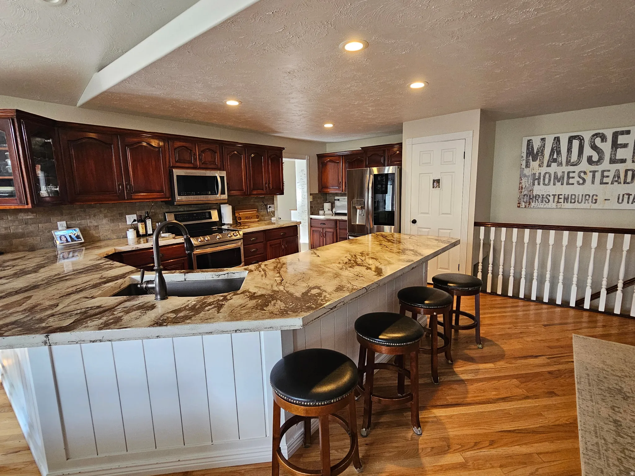 Kitchen with a peninsula, appliances with stainless steel finishes, a textured ceiling, a breakfast bar, and recessed lighting