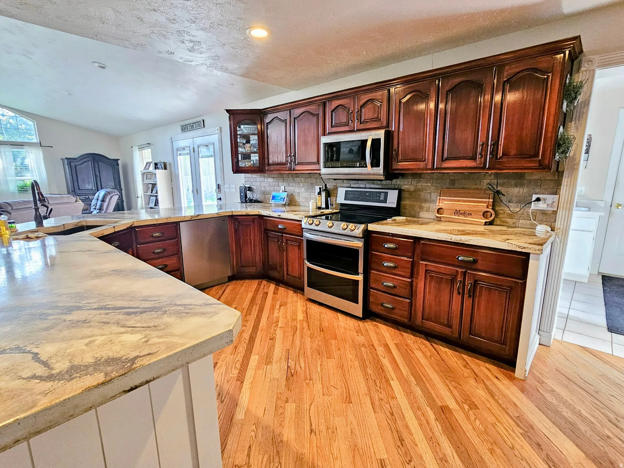 Kitchen with stainless steel appliances, backsplash, light stone countertops, light wood-style floors, and a textured ceiling