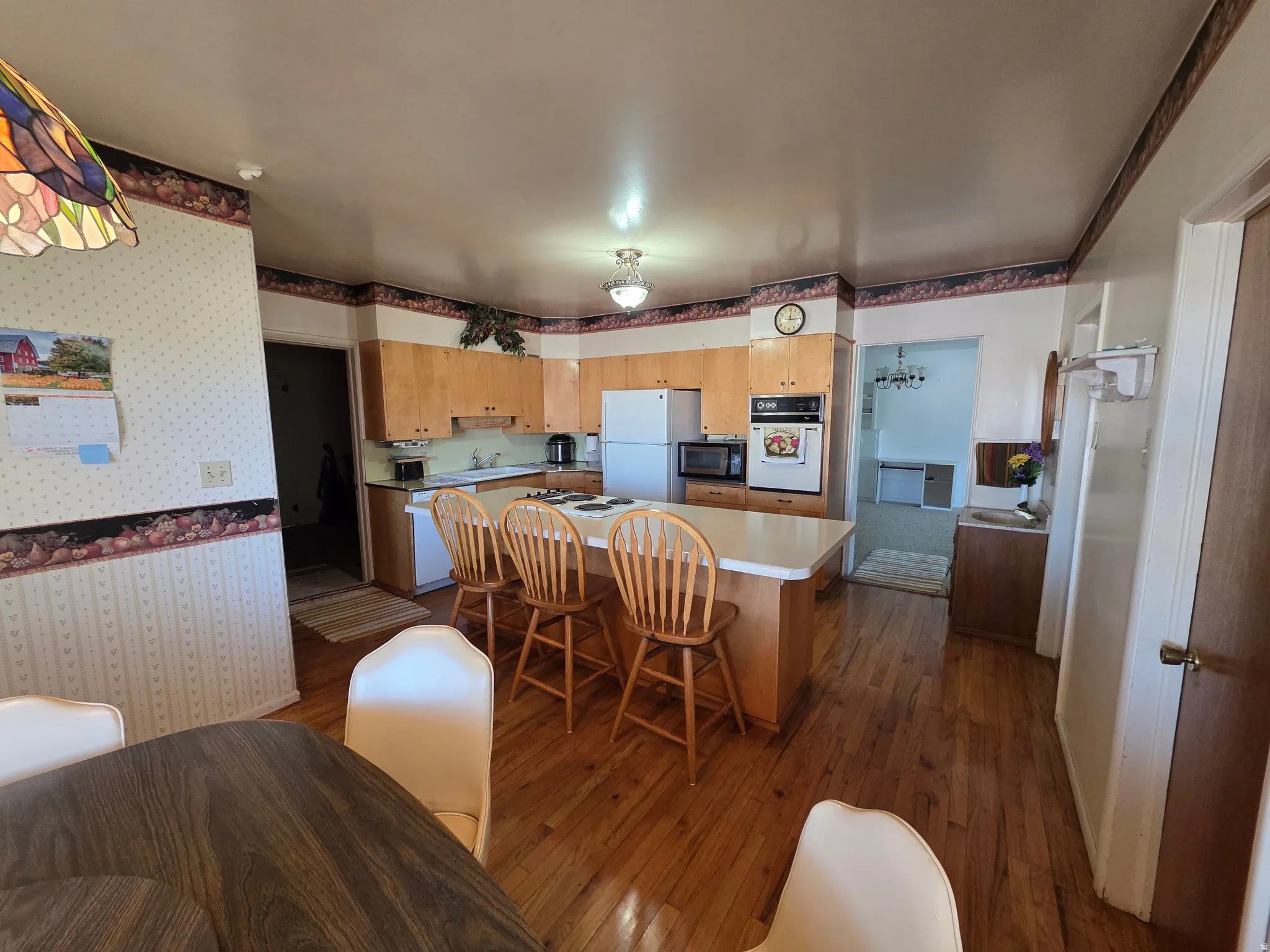 Kitchen featuring dark wood-style floors, light countertops, white appliances, a center island, and a breakfast bar