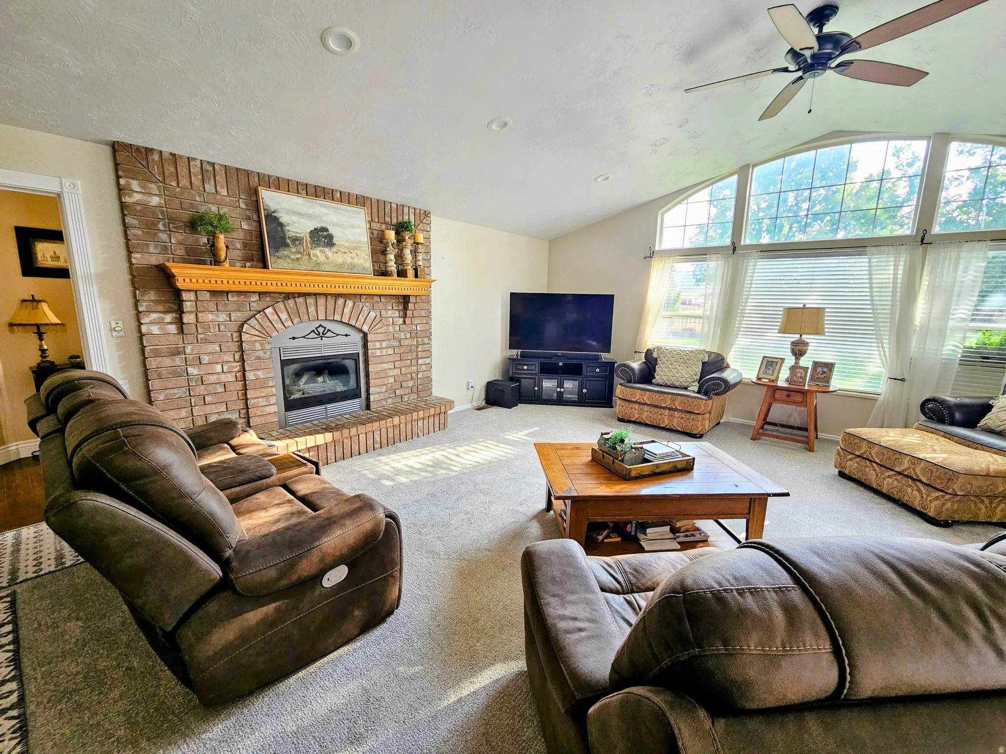 Living room with lofted ceiling, a brick fireplace, carpet floors, and ceiling fan