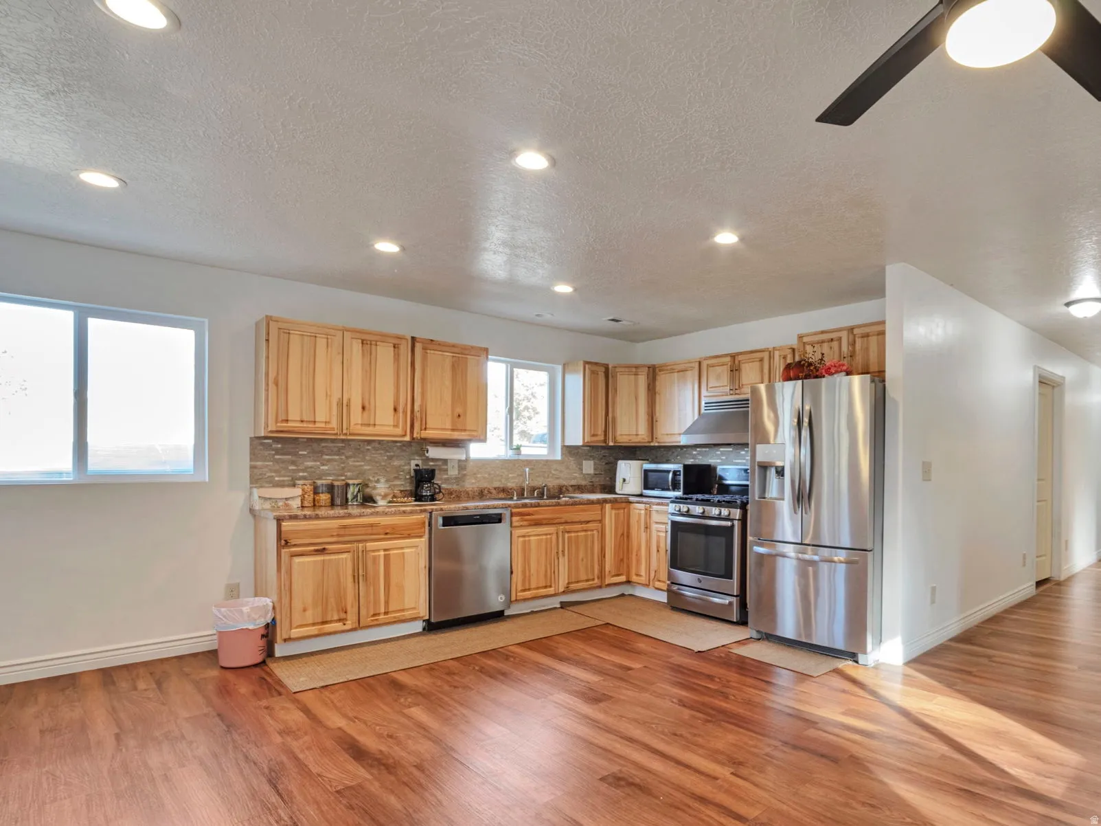 Kitchen featuring appliances with stainless steel finishes, tasteful backsplash, a textured ceiling, light wood finished floors, and recessed lighting