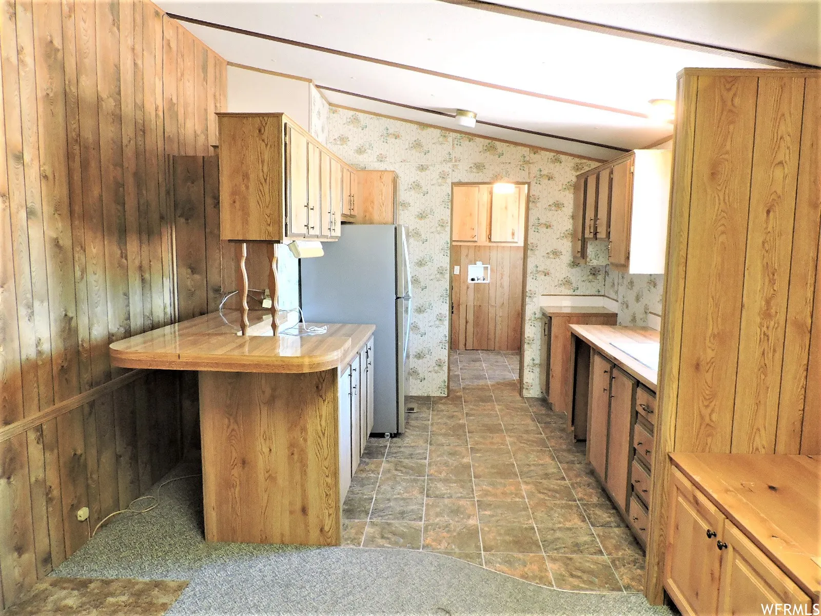 Kitchen with vaulted ceiling, freestanding refrigerator, brown cabinetry, a peninsula,