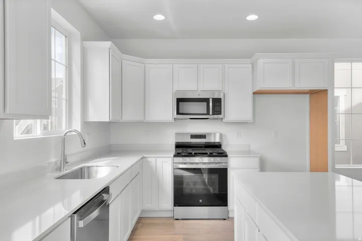 Kitchen featuring appliances with stainless steel finishes, white cabinetry, light wood-style floors, recessed lighting, and light stone countertops