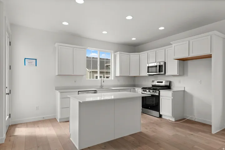 Kitchen featuring appliances with stainless steel finishes, white cabinets, light wood finished floors, recessed lighting, and a center island
