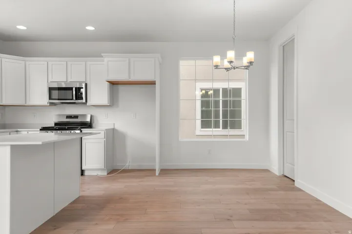 Kitchen with white cabinets, hanging light fixtures, stainless steel appliances, a chandelier, and light wood-type flooring