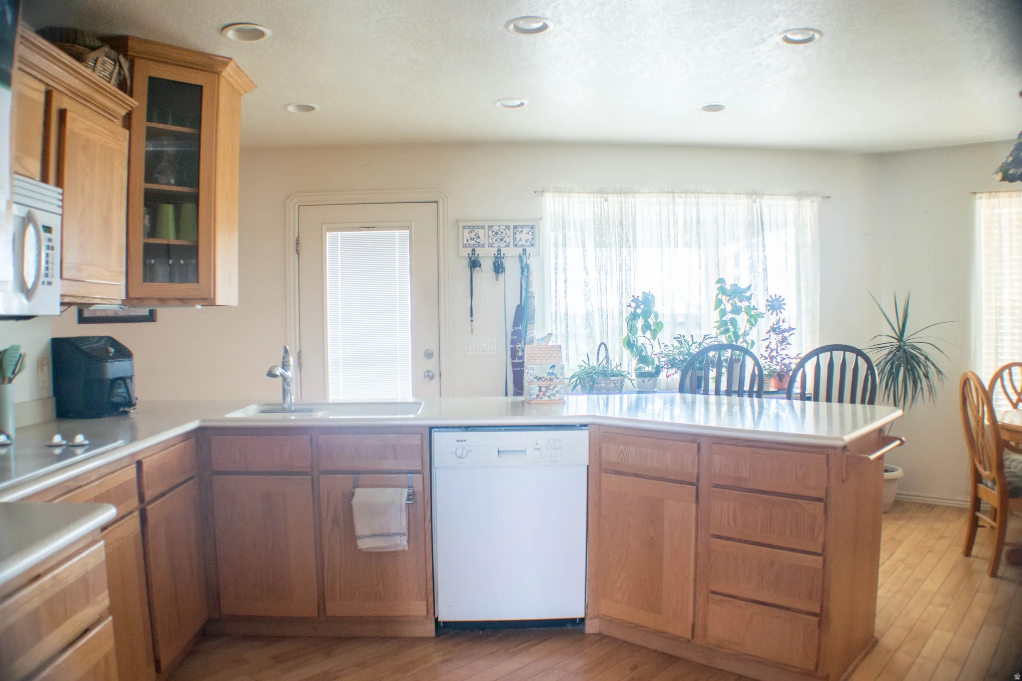Kitchen featuring white appliances, light countertops, brown cabinets, glass insert cabinets, and recessed lighting