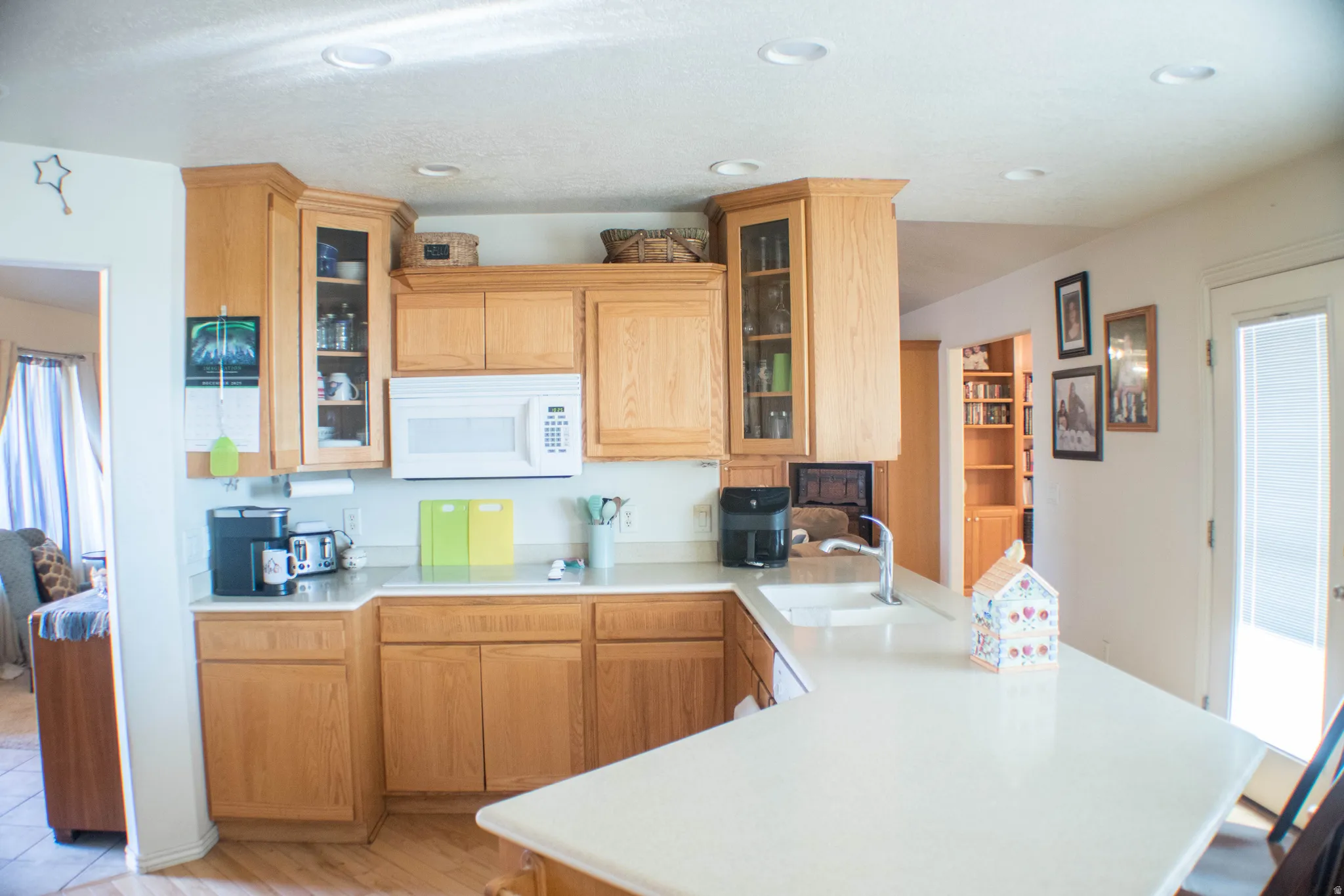 Kitchen featuring glass insert cabinets, light countertops, white microwave, a peninsula, and recessed lighting