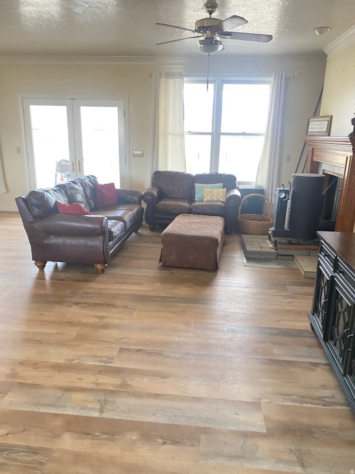 Living room featuring ornamental molding, a textured ceiling, light wood-style flooring, a ceiling fan, and a fireplace
