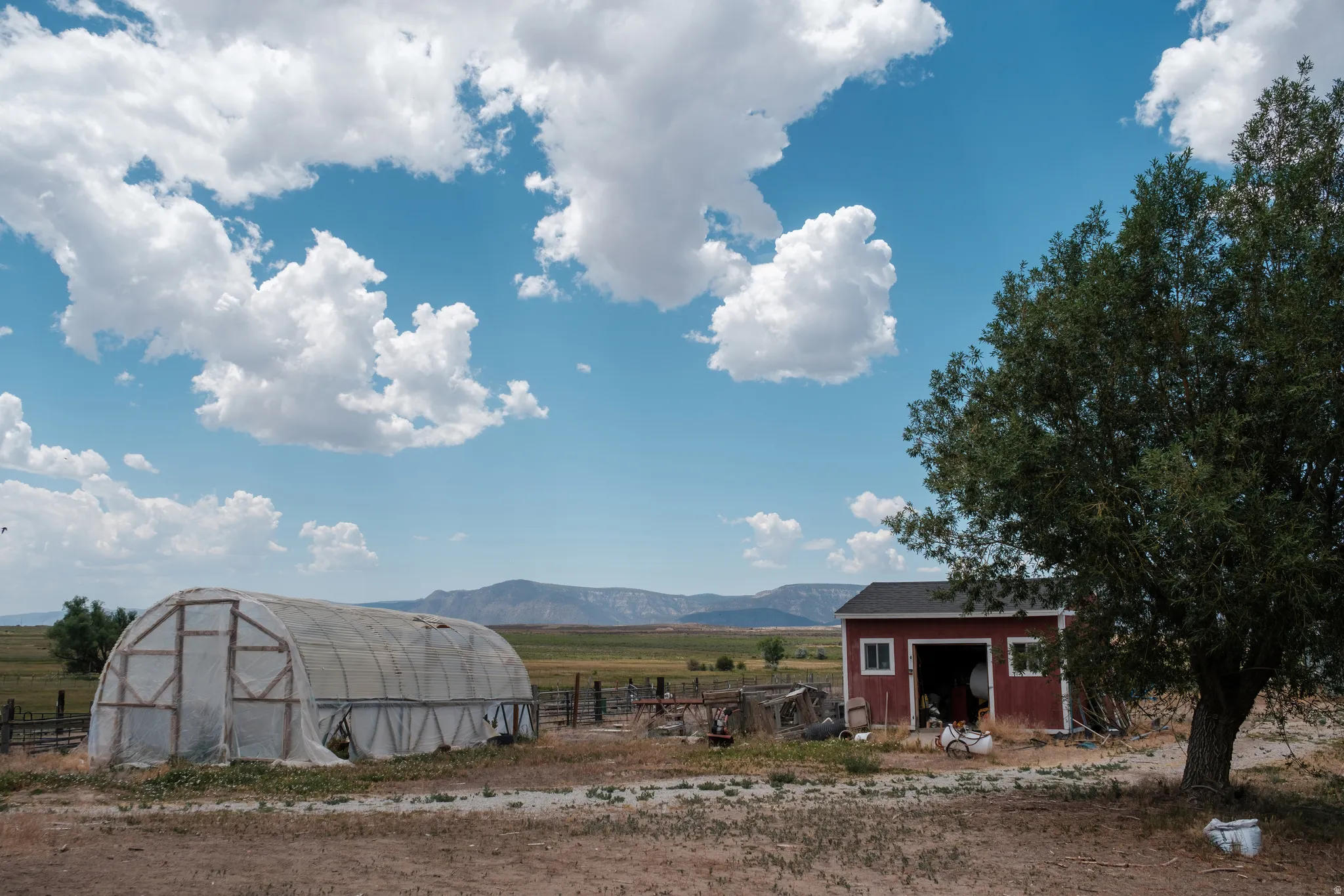 Rural property featuring a greenhouse structure, a red outbuilding with white trim, and mature landscaping