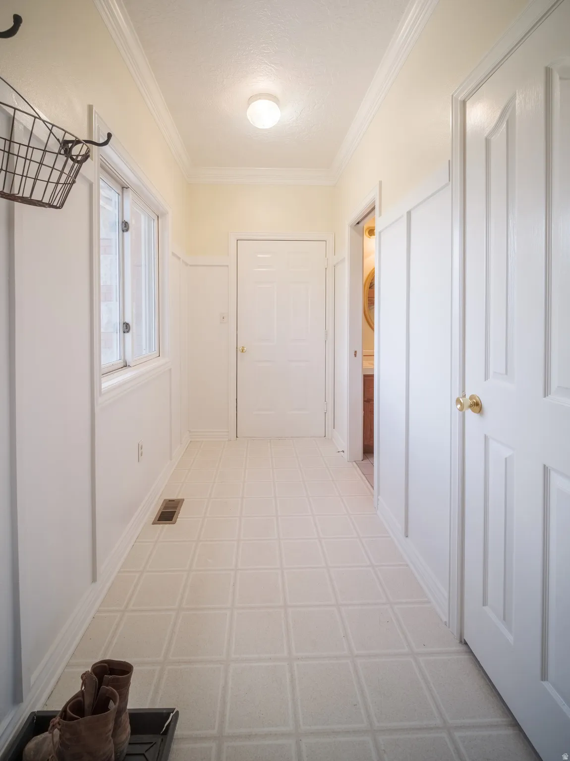 Hallway featuring light-toned flooring, white wainscoting, and crown molding
